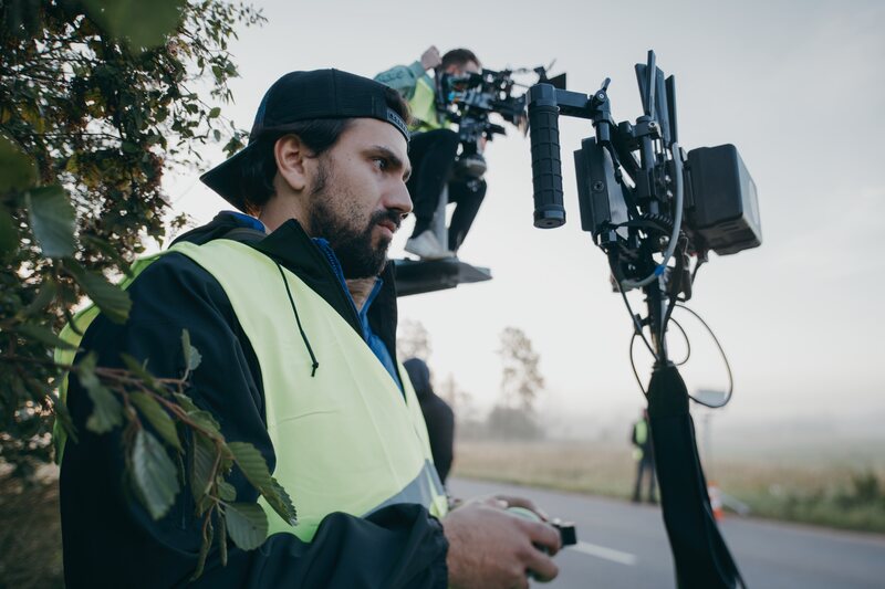 Crew member with a wireless handset beside a cinema camera on a crane at dawn.
