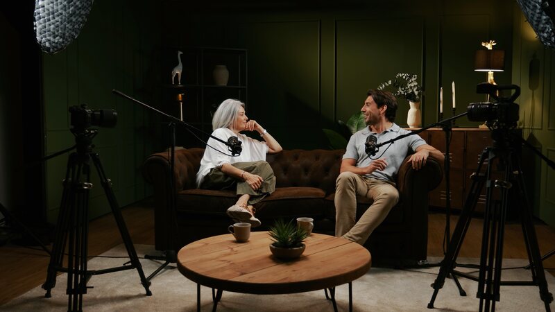 Two cameras on tripods and two boom microphones covering a conversation on a sofa.